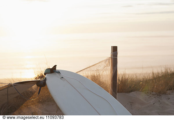 Upside down surfboard leaning against fence during sunset