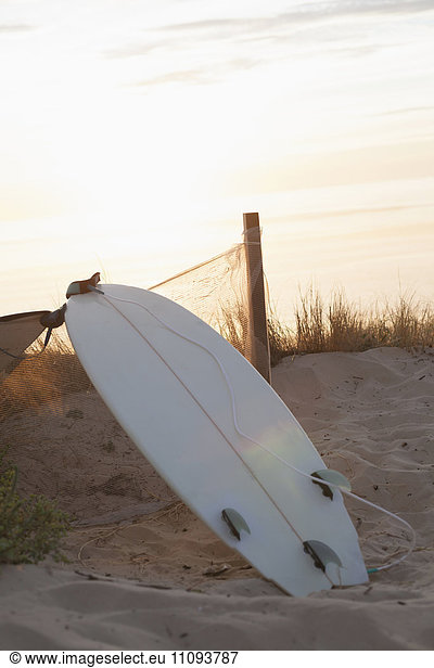 Upside down surfboard leaning against fence during sunset