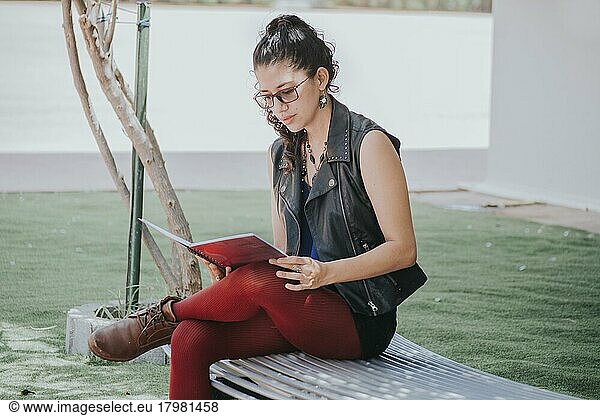 Urban girl sitting on a bench reading a book  Latin girl reading a book outside  concept of a student girl reading a book