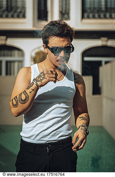 Urban portrait of a tattooed guy smoking a cigarette outdoors