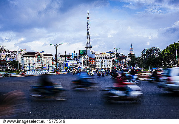 Urban scene with blurred motion of passing traffic and motorbikes on wide street.