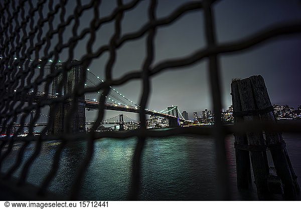 USA  New York  New York City  Kettengliedzaun gegen beleuchtete Brooklyn Bridge bei Nacht