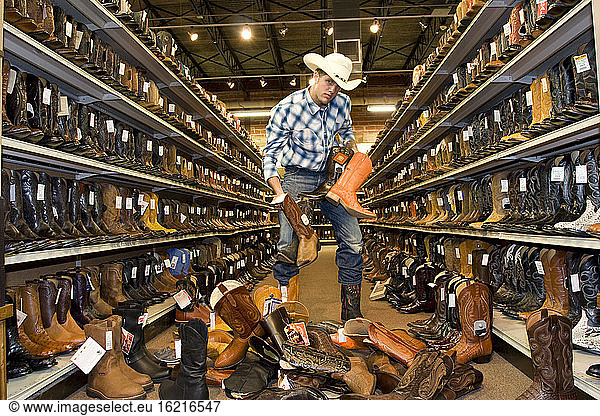 USA  Texas  Dallas  Young man choosing cowboy boots in shoe store