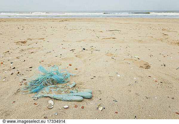 Used disposable glove and other waste polluting sandy coastal beach