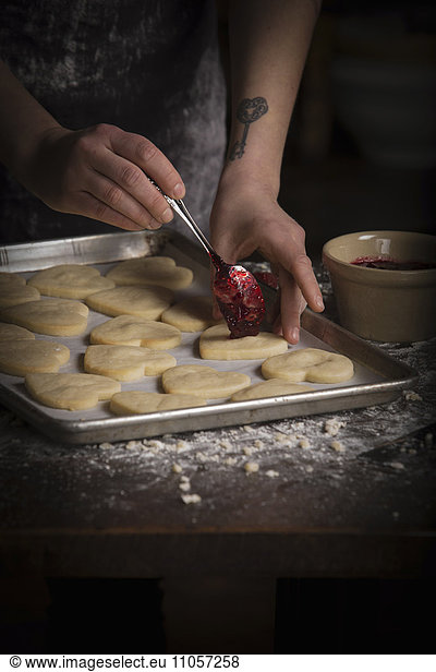 Valentine's Day baking,  woman spreading raspberry jam on heart shaped biscuits.