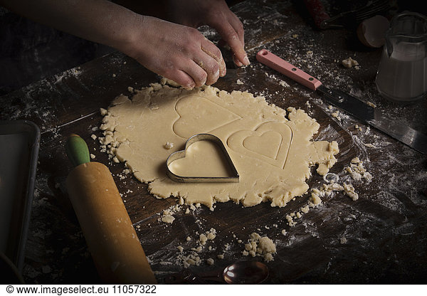 Valentine's Day baking. Woman cutting out heart shaped biscuits from dough on a floured surface.