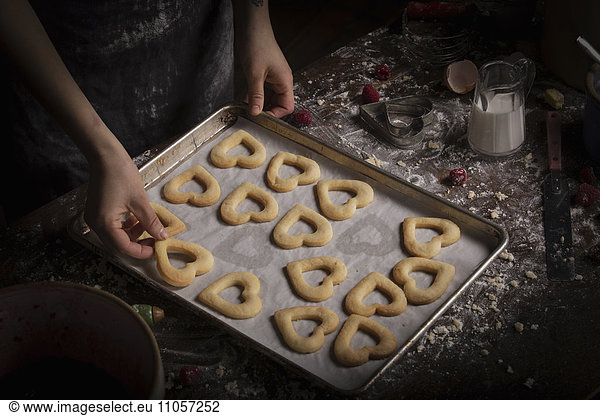 Valentine's Day baking  woman arranging heart shaped biscuits on a baking tray.