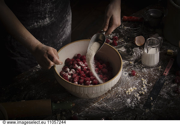 Valentine's Day baking  woman preparing fresh raspberries in a bowl  adding sugar.