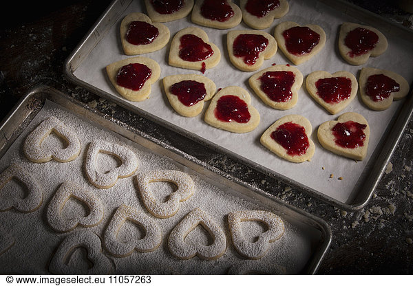 Valentine's Day baking  woman spreading raspberry jam on heart shaped biscuits.