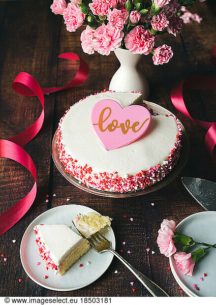 Valentine's Day cake with heart sprinkles and flowers on wooden table.
