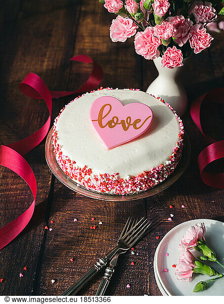 Valentine's Day cake with heart sprinkles and flowers on wooden table.