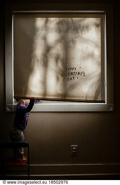 Valentine's Day image of child peeking out of window in morning light