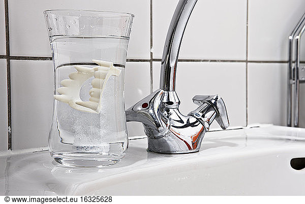 Vampire dentures in water glass on bathroom sink