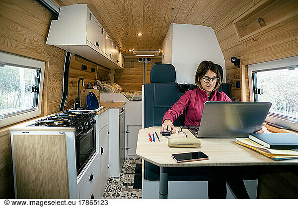 Vanlife. Woman doing remote work with the computer in the motorhome.
