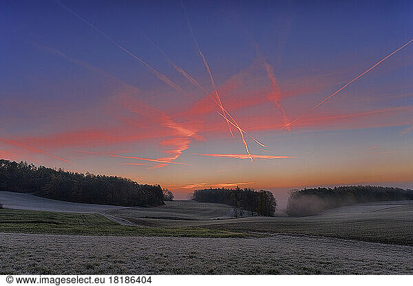 Vapor trails stretching over countryside field at foggy dawn