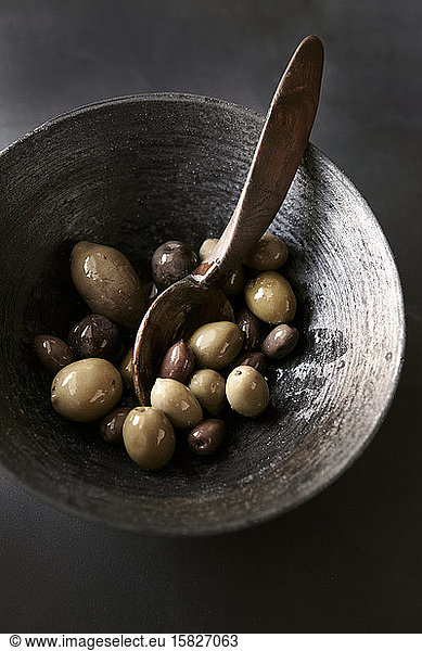 Variety of olives in black bowl with spoon