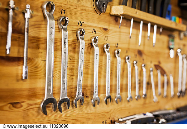 Various sizes of spanners hanging on wooden wall at workshop