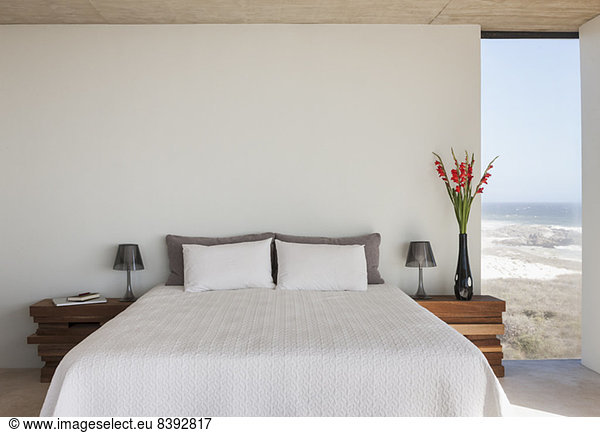 Vase of flowers next to bed in bedroom with ocean view