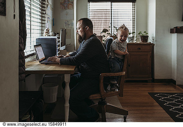 Vater arbeitet von zu Hause aus mit einem einjährigen Jungen  der bei der Arbeit weint