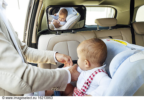 Vater befestigt Baby im Kindersitz im Auto