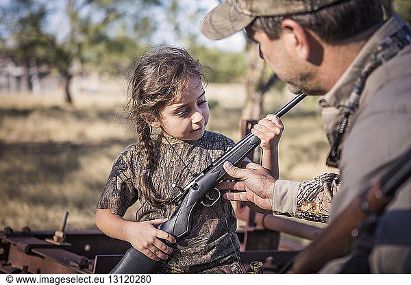 Vater führt Mädchen mit Gewehr in der Hand