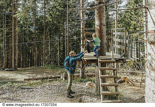 Vater hält Tier  während Sohn im Wald Seilgarten macht