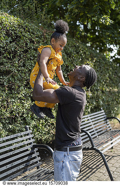Vater hebt Tochter auf einer Parkbank hoch