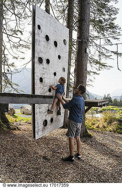 Vater hilft seiner kleinen Tochter beim Klettern an einer kleinen Waldkletterwand