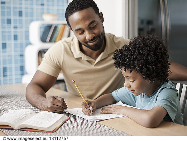 Vater hilft Sohn bei den Hausaufgaben bei Tisch zu Hause