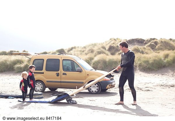 Vater mit zwei Söhnen  Surfbrett und Auto am Strand