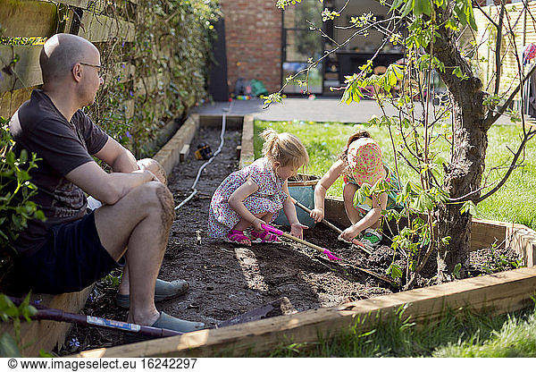 Vater schaut Kindern beim Graben im Garten zu