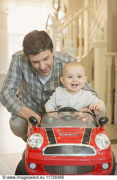 Vater schiebt fröhliches  süßes Baby im Spielzeugauto
