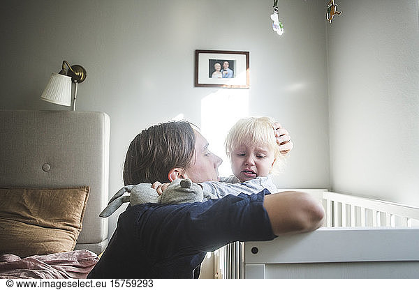 Vater tröstet weinendes blondes Baby in der Krippe mit zärtlicher Liebe zu Hause
