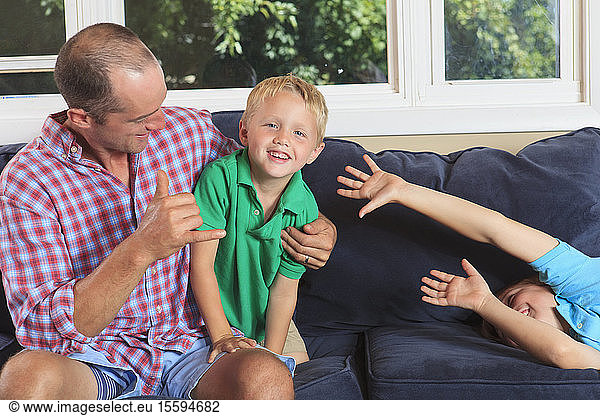 Vater und Söhne mit Hörbehinderungen gebärden auf ihrer Couch play in amerikanischer Zeichensprache