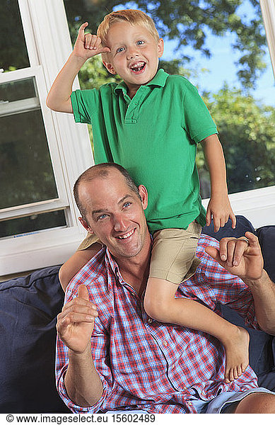 Vater und Sohn mit Hörbehinderung gebärden Cowboy  play in amerikanischer Zeichensprache auf ihrer Couch
