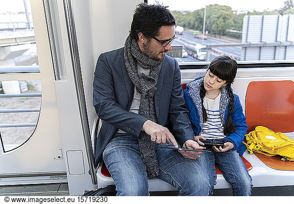 Vater und Tochter in der U-Bahn und mit Tablet und Smartphone