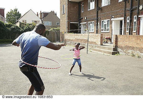 Vater und Tochter spielen mit Plastikreifen in sonniger Nachbarschaft