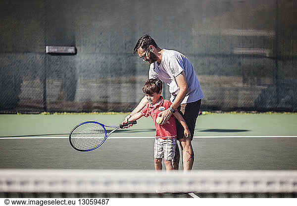 Vater unterrichtet Sohn Tennis auf dem Platz