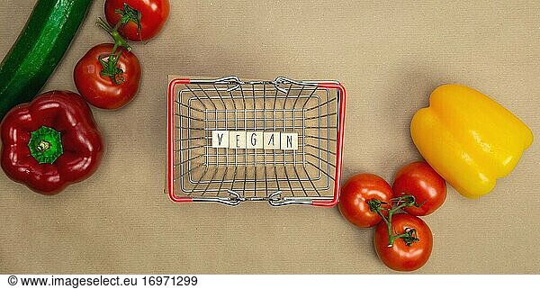 Vegan geschrieben auf Holzwürfeln umgeben mit Gemüse in Einkaufskorb Draufsicht mit Handwerk Papier Hintergrund  Vegan  Gesunde Ernährung  Vegetarier Konzept  Kopie Raum Lebensstil.
