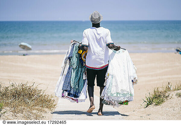 Vendor with dresses for sale walking on boardwalk at beach