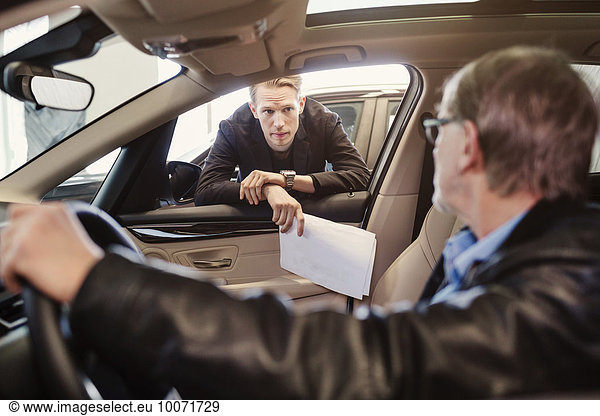 Verkäufer beim Anblick eines älteren Mannes  der in einem Autohaus sitzt