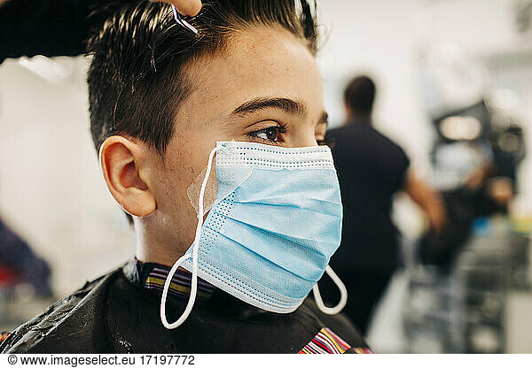 Verklemmter Teenager mit Maskenband beim Haarschnitt im Salon