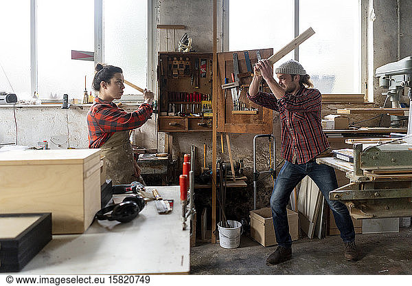 Verspielte Handwerkerin und Handwerker kämpfen in ihrer Werkstatt
