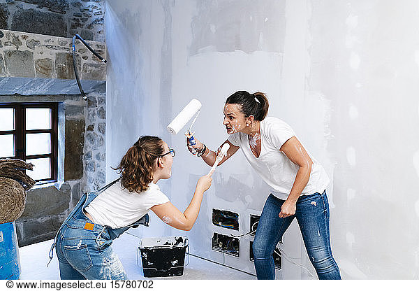 Verspielte Mutter und Tochter amüsieren sich beim Streichen einer Wand ihres neuen Hauses