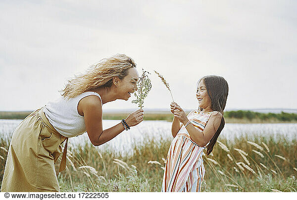 Verspielte Mutter und Tochter halten Zweige am See