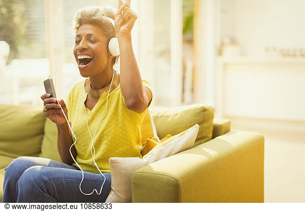 Verspielte reife Frau hört Kopfhörer mit MP3-Player im Wohnzimmer