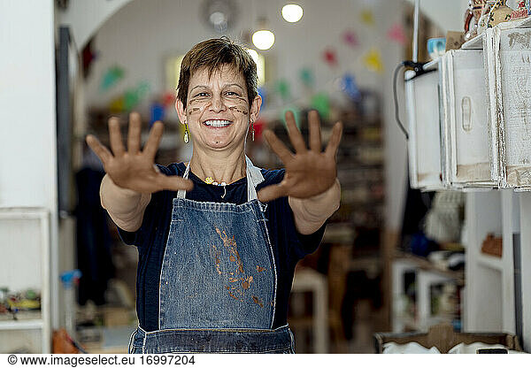 Verspielter Künstler mit schmutzigen Händen in Ton im Keramikgeschäft
