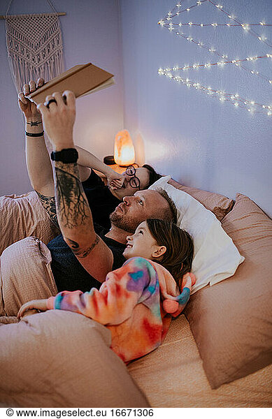 vertical image of father laying in bed reading to kids