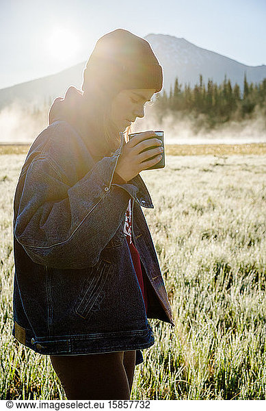 Vertical image of young woman holding reusable cup at sunrise