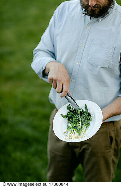 Vertical photo of man using tongs to toss the wild ramps on a platter